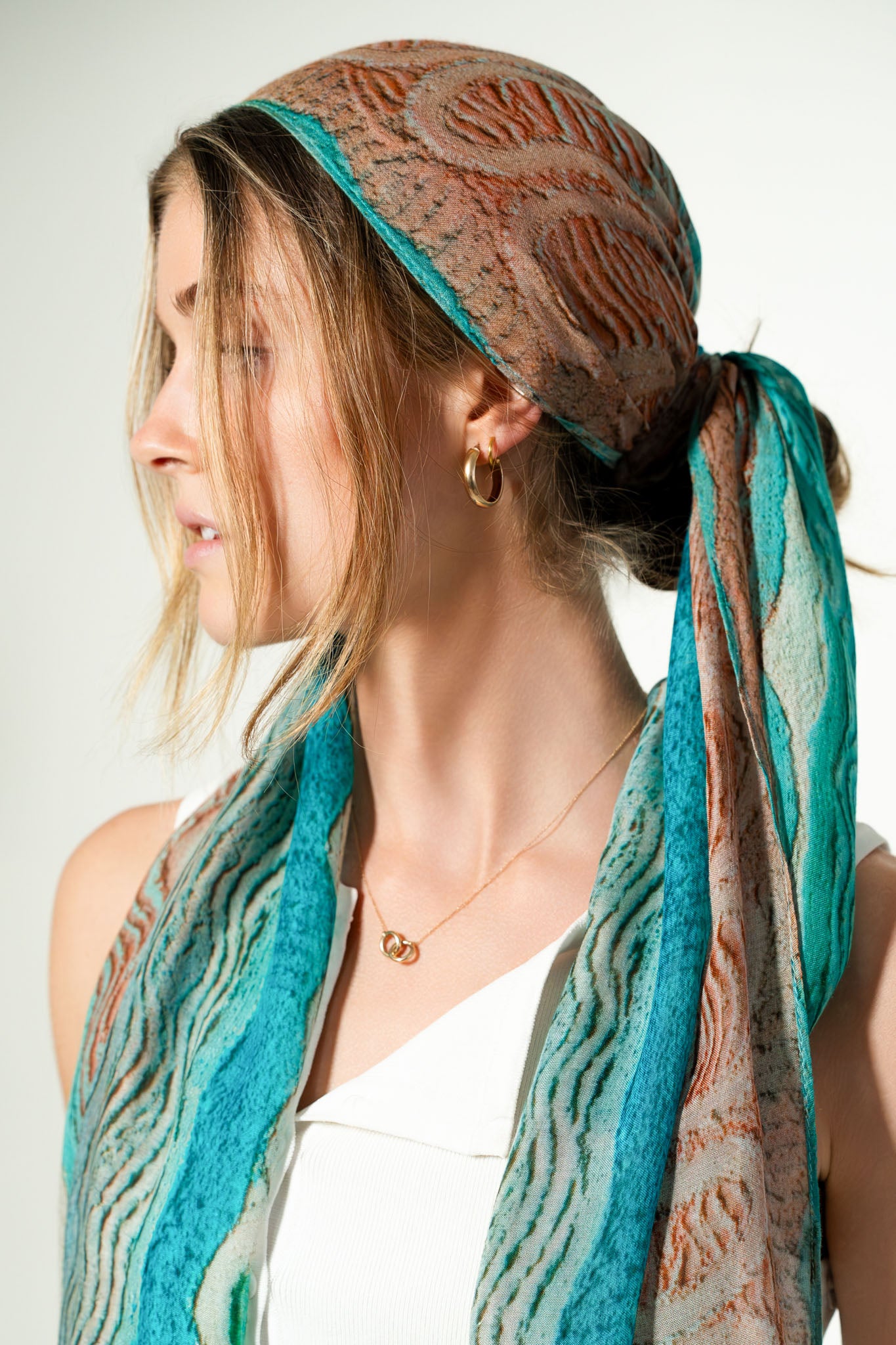 Woman wearing a patterned headscarf and scarf with a neutral background